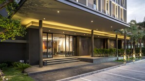 A modern hotel entrance with a covered outdoor seating area, steps leading to the entrance, and a parking lot. - Xotel (Khon Kaen)