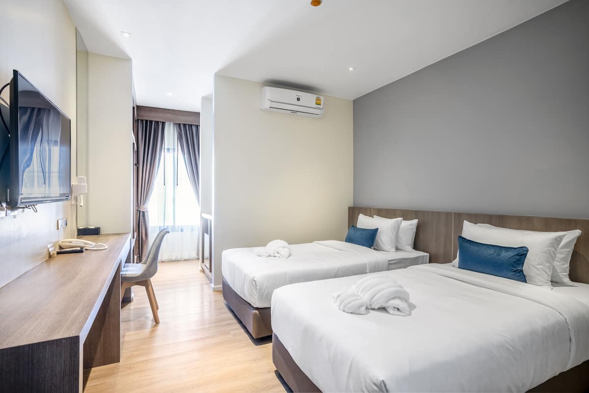 A hotel room with two beds, a desk, a chair, and an air conditioning unit.