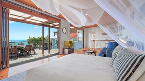 A bedroom with a large bed, a balcony with a table and chairs, and a view of the ocean. - Boatshed Waterfront Huskisson (Huskisson)