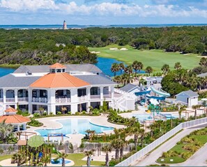 A large resort with multiple swimming pools, a golf course, and a lighthouse in the background.