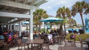 An outdoor patio area with tables and chairs, palm trees, and umbrellas.