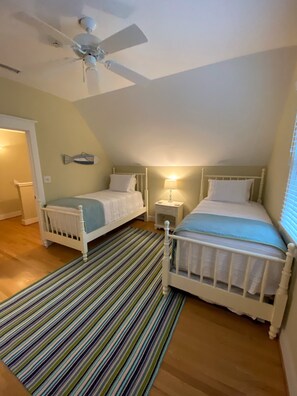A bedroom with two single beds, a striped rug, a ceiling fan, and a nightstand with a lamp.