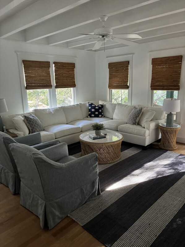 A living room with a sectional sofa, grey armchairs, a coffee table, and a ceiling fan.