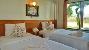 Habitación de hotel con dos camas, cada una con sábanas blancas y almohadas estampadas con motivos florales. Hay una lámpara de pared sobre las camas y un cuadro de flores en la pared.