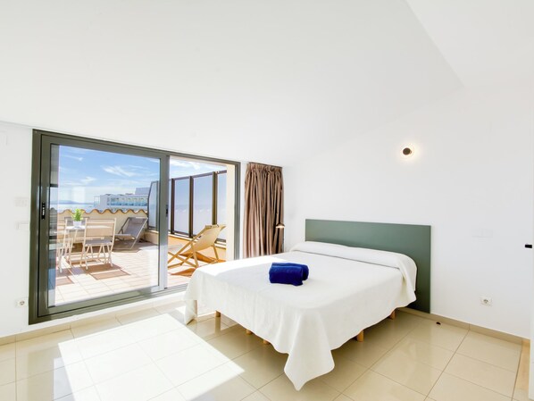 Une chambre d’hôtel comprenant un lit, une petite table, une chaise et une porte-fenêtre coulissante donnant sur un espace extérieur avec une table et des chaises.