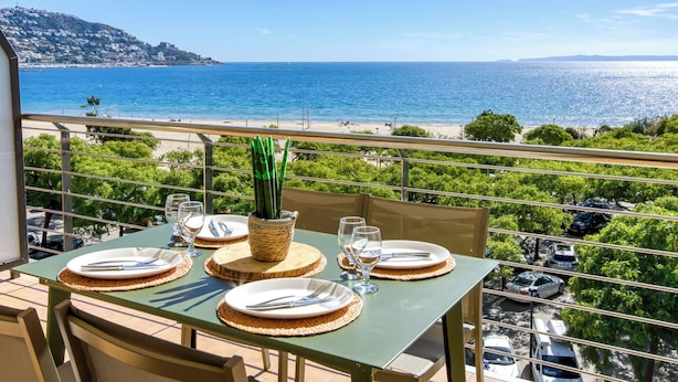 A balcony table set with plates, cutlery, and glasses, overlooking a beach and the sea. - Mileni I by Interhome (Roses)