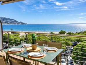 Une table de balcon, dressée avec des assiettes, des couverts et des verres, donnant sur une plage et la mer.