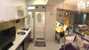 A compact kitchen with a built-in oven, a sink, and a TV. There's a dining area with a table and chairs, and a small washing machine. - Dongqu Light Inn (Taipei)