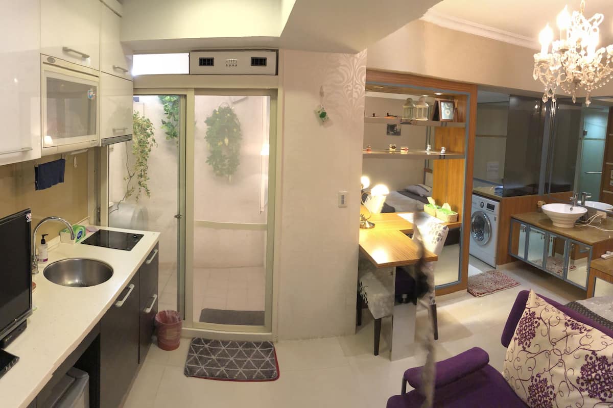Cozinha compacta com forno embutido, pia e televisão. Possui área de refeições com mesa e cadeiras, além de uma máquina de lavar roupa pequena.