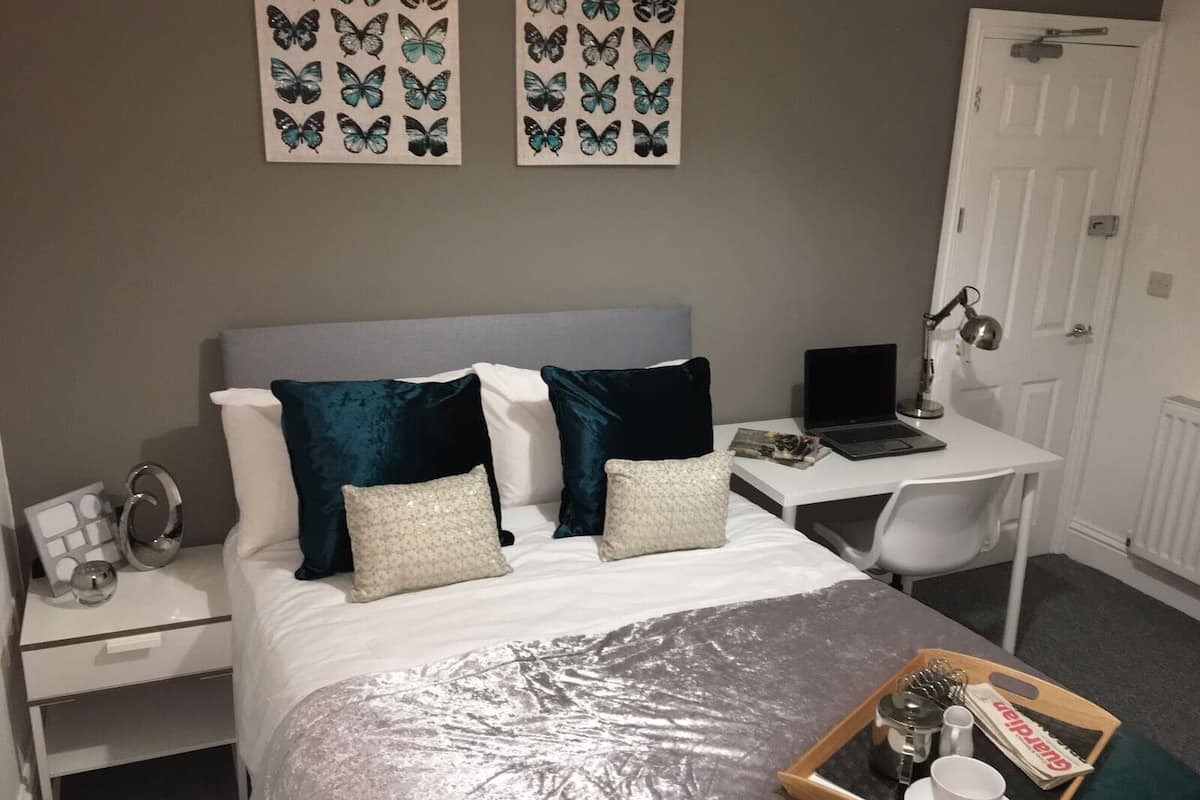 A neatly arranged bedroom with a bed, bedside tables, a desk, and a laptop.