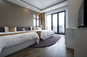 Habitación de hotel moderna con dos camas, un ventanal grande, balcón y televisor de pantalla plana.