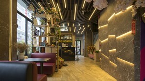L’intérieur d’une auberge de jeunesse moderne, avec des espaces de détente, un comptoir d’accueil et une enseigne indiquant le nom de l’auberge.