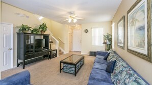 A living room with a dark wooden entertainment center, a blue sofa, a glass coffee table, and a ceiling fan. - Bridgewater_at_town_center_233 (Davenport)