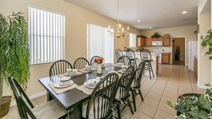A dining area with a table set for six, surrounded by chairs, and a kitchen in the background. - Bridgewater_at_town_center_233 (Davenport)