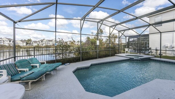 A covered outdoor swimming pool with lounge chairs and a table, surrounded by a metal fence and a view of houses in the background. - Bridgewater_at_town_center_233 (Davenport)