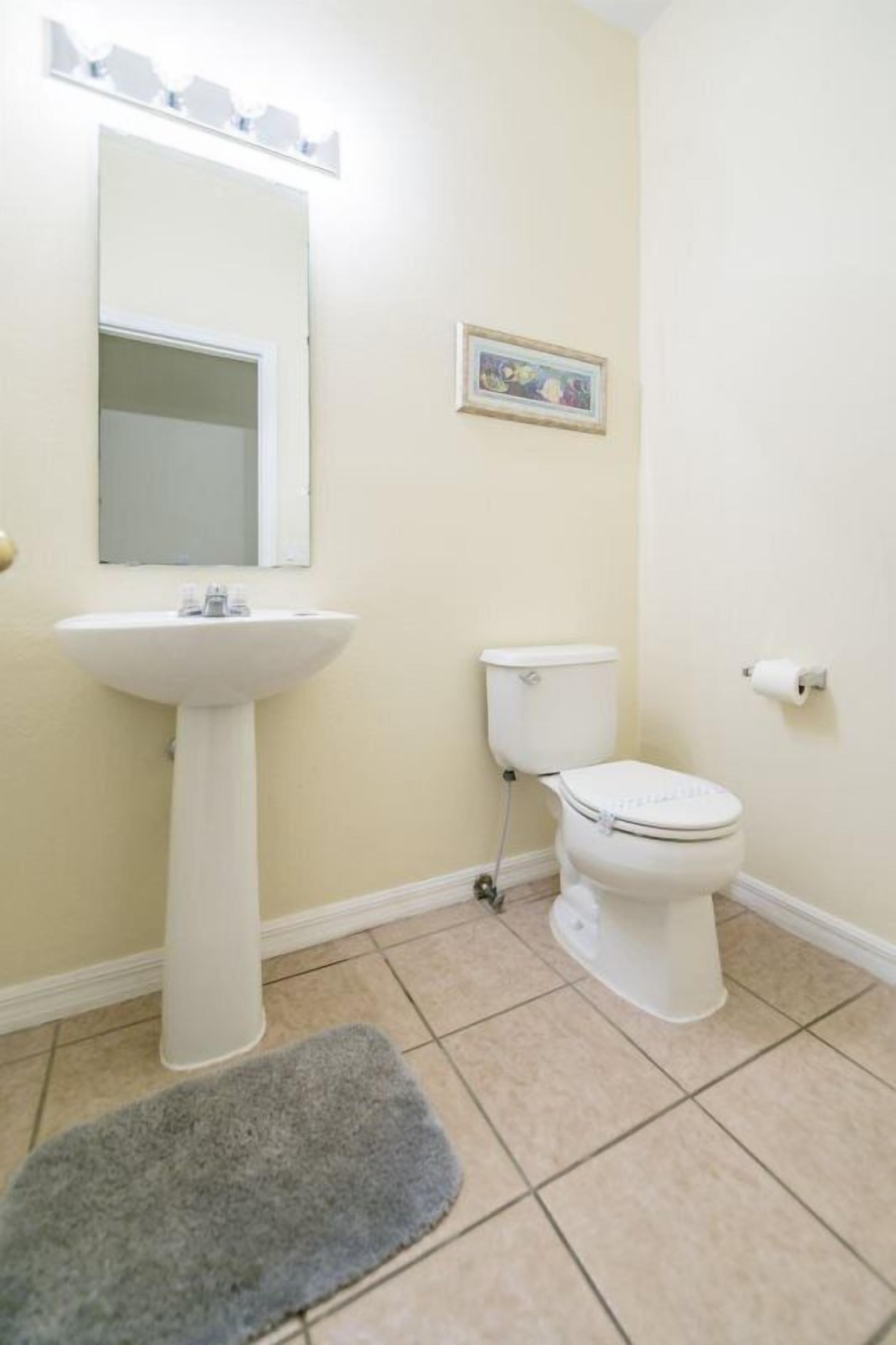 A bathroom with a pedestal sink, toilet, and a small rug on the floor.
