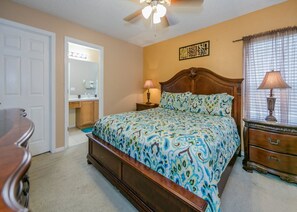 A bedroom with a bed, bedside tables, a dresser, a ceiling fan, and a bathroom visible through an open door. - Emerald_island_2761 (Kissimmee)