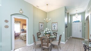 A dining area with a round table, wicker chairs, and a chandelier. - Windsor_palms_8144 (Kissimmee)