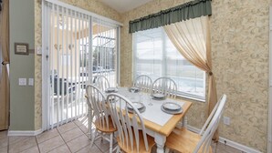 A dining area with a table set for four, white chairs, a window with curtains, and a door with a view of the outside. - Windsor_palms_8144 (Kissimmee)