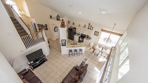 A spacious living area with a large TV, leather sofas, a kitchen with a central island, and a staircase leading to an upper floor. - Windsor_palms_8169n (Kissimmee)