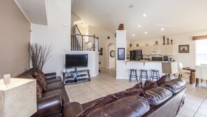 A spacious living area with a large leather sofa, a flat-screen TV, and a kitchen with a central island and bar stools. - Windsor_palms_8169n (Kissimmee)