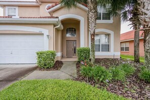 A two-story house with a garage, a front door, and a well-maintained lawn with shrubs and flowers.