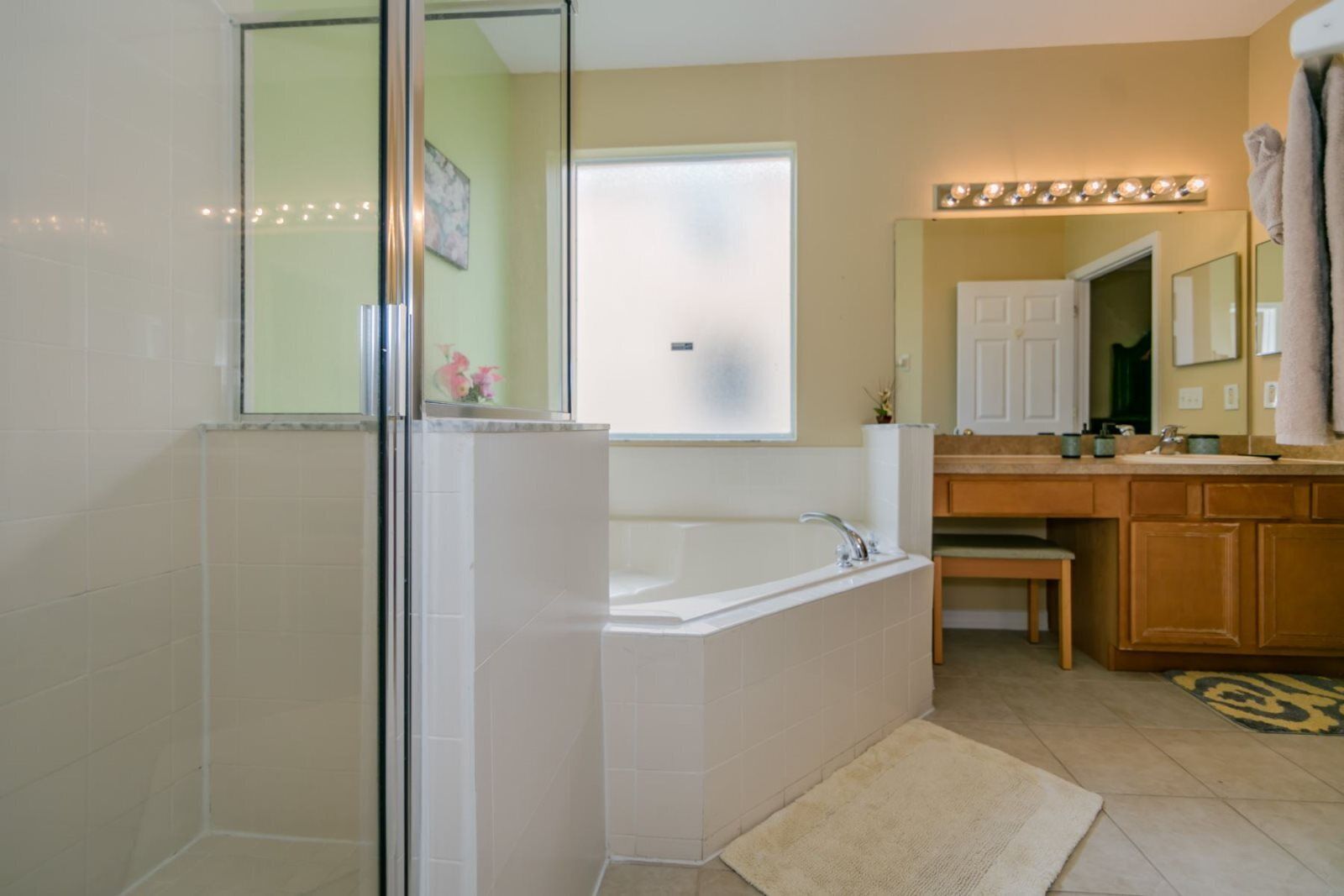 Un baño moderno con cabina de ducha de vidrio, bañera independiente, tocador con espejo y lavamanos.