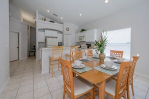 A modern kitchen with white cabinets, a central island, and a dining area with a wooden table and chairs. - Glenbrook_16643 (Clermont)