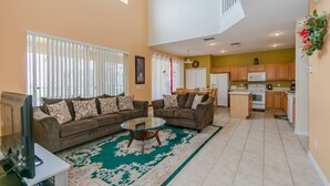 A spacious living room with two sofas, a coffee table, and a TV. There is a kitchen area with wooden cabinets and a microwave. - Emerald_island_2703 (Kissimmee)