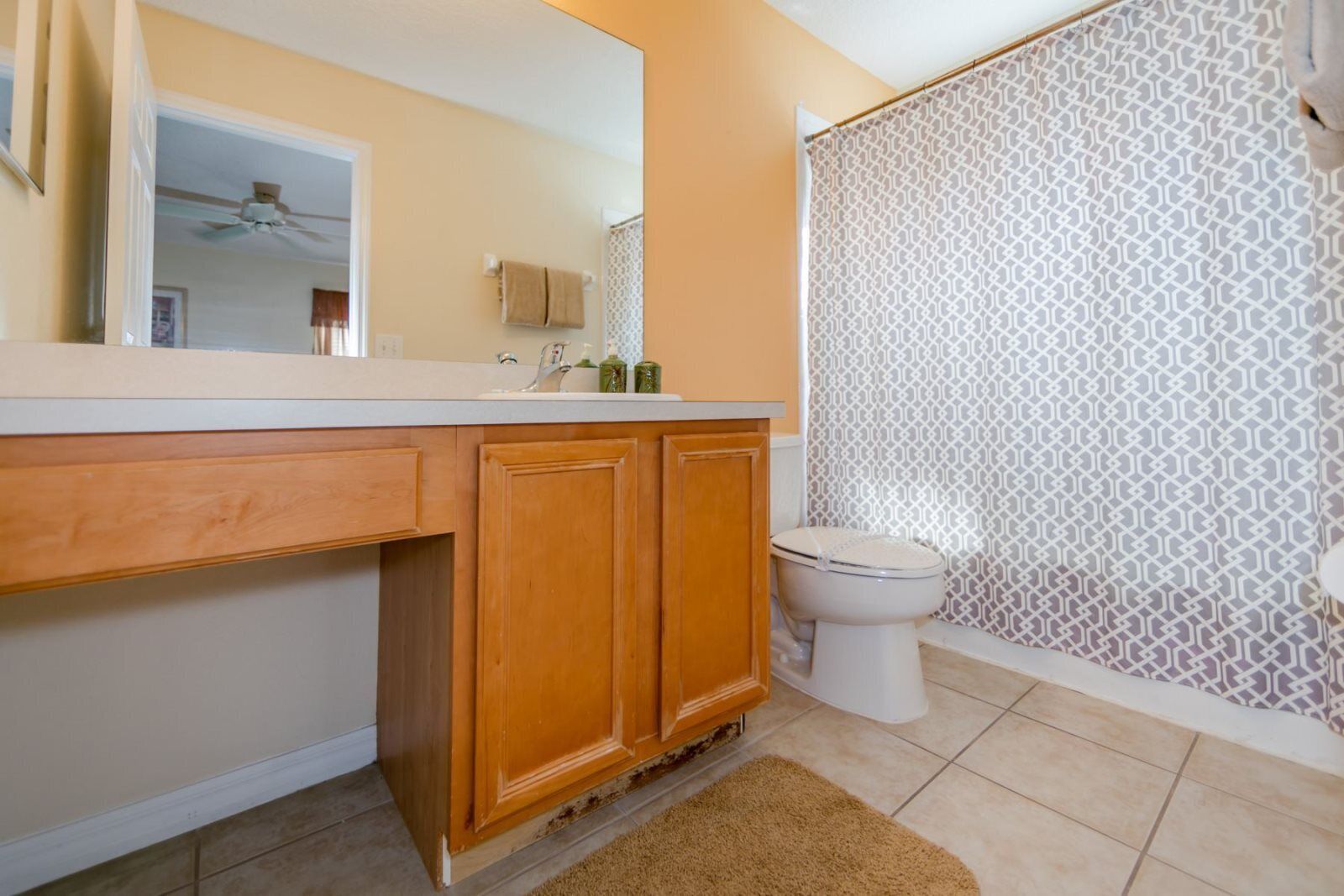 A bathroom with a wooden vanity, a white toilet, and patterned shower curtains.