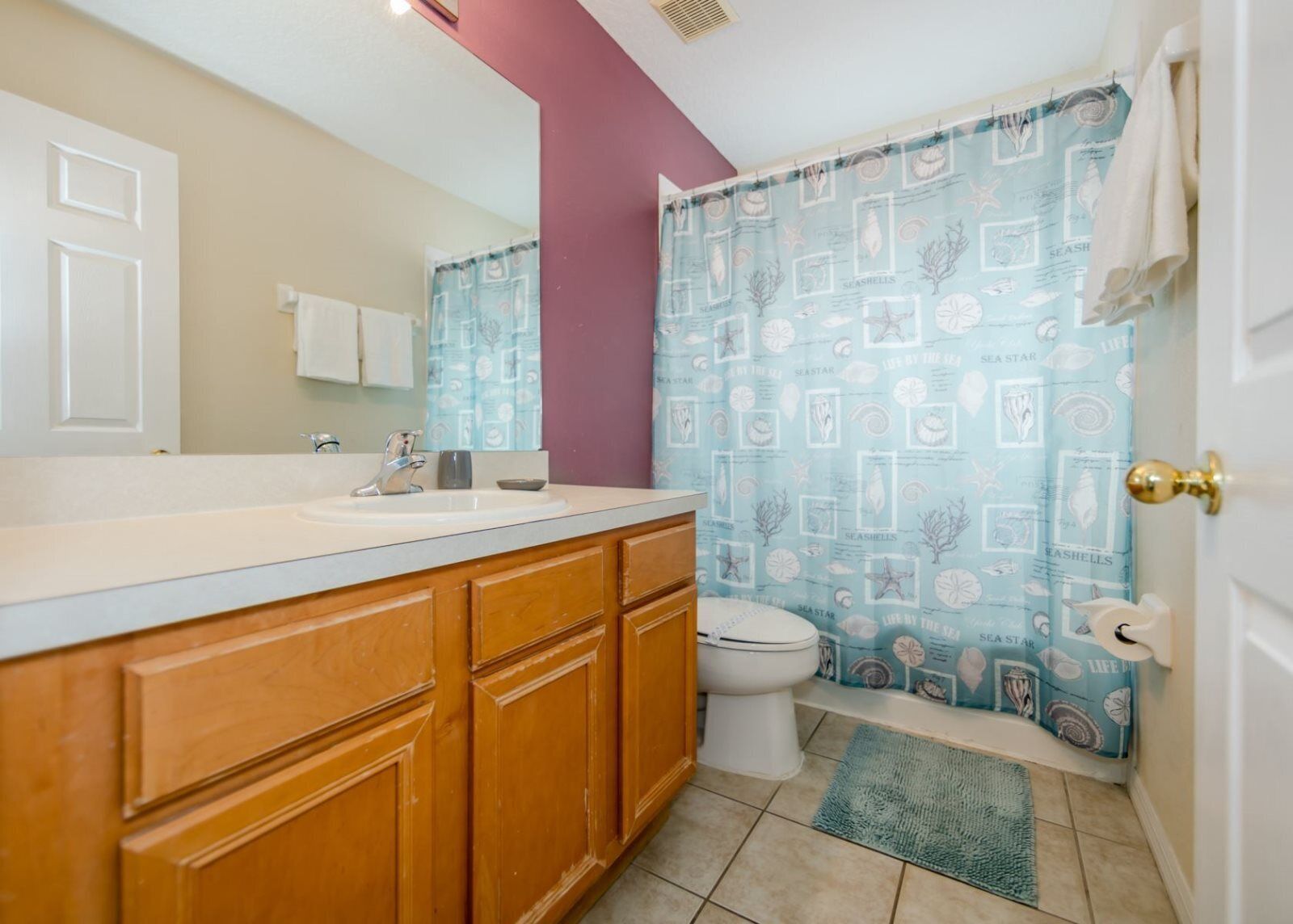 A bathroom with a wooden vanity, a white sink, a toilet, and a shower curtain with a sea-themed pattern.
