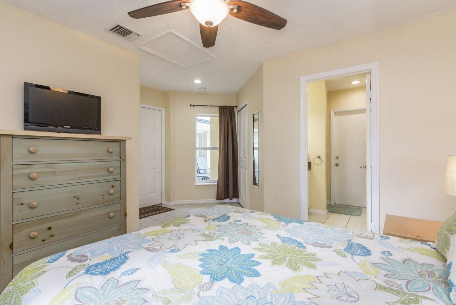 Une chambre à coucher comprenant un lit, une commode, un ventilateur de plafond et un téléviseur posé sur la commode.