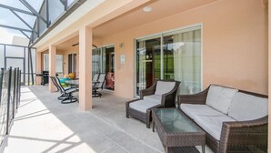 A covered outdoor seating area with wicker furniture, a table, and a glass partition. - Emerald_island_8640 (Kissimmee)