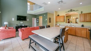 A spacious living room with a large sofa, a dining table with chairs, a kitchen area with wooden cabinets, and a small balcony. - Emerald_island_8640 (Kissimmee)