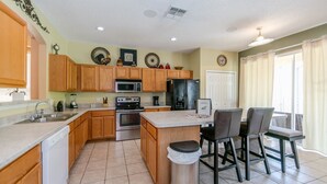 A modern kitchen with wooden cabinets, stainless steel appliances, and a dining area with chairs. - Emerald_island_8640 (Kissimmee)