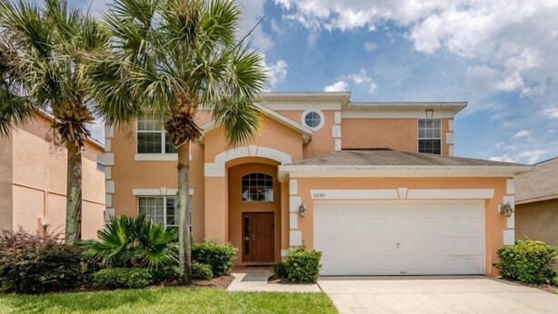 A two-story house with a garage, a front entrance with a door, and a driveway. - Emerald_island_8640 (Kissimmee)