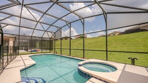 A covered swimming pool with a hot tub, surrounded by a metal frame and a grassy lawn. - Emerald_island_8640 (Kissimmee)