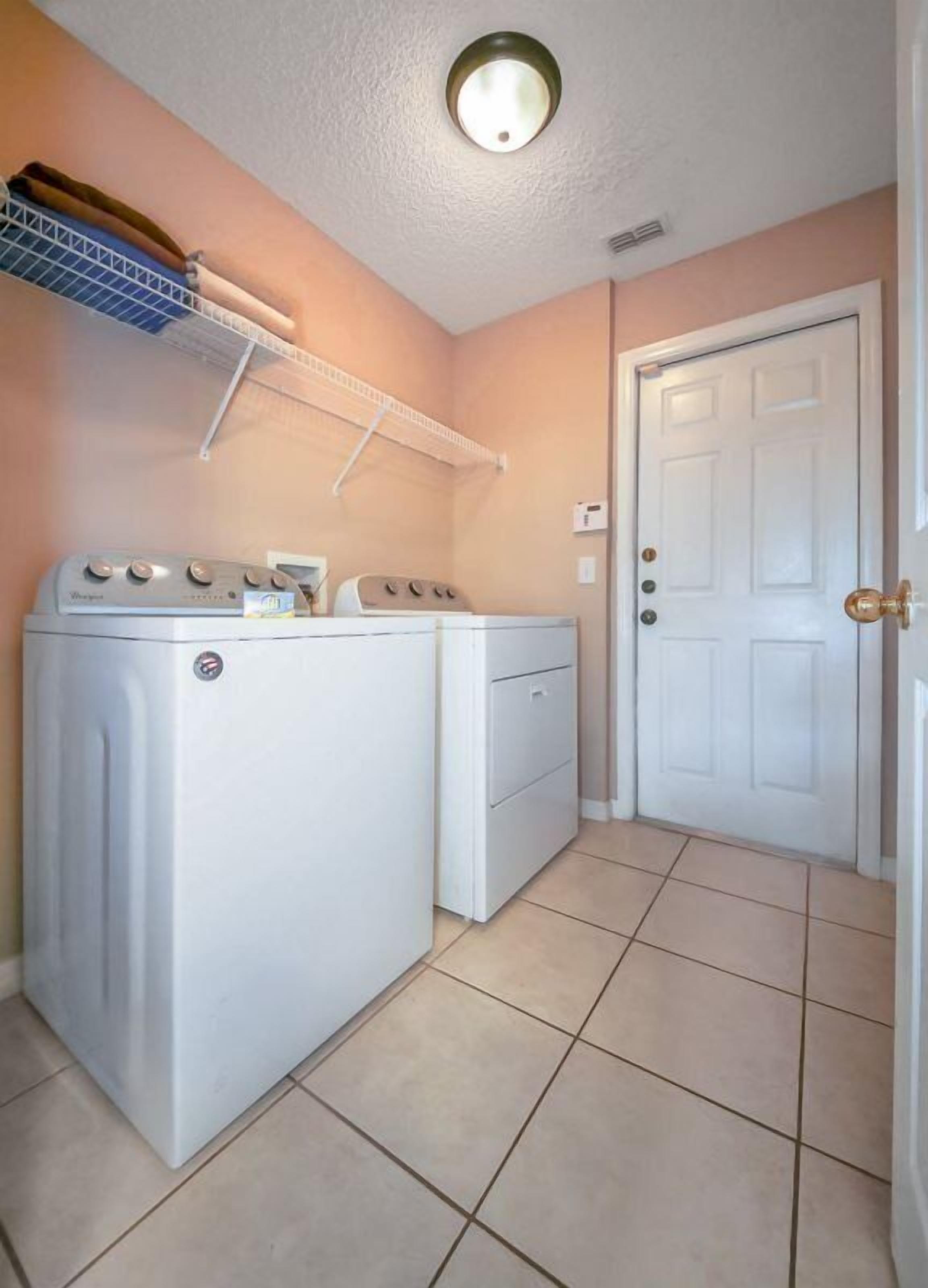 A laundry room with a washer and dryer, a shelf above the washer, and a white door.
