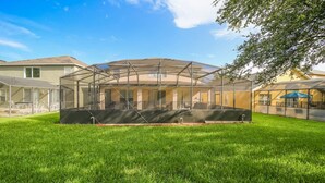 A covered outdoor area with a lawn, a grill, and a table. - Emerald_island_8520 (Kissimmee)