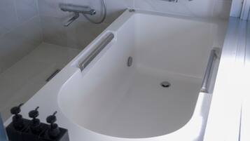 A modern bathroom with a white bathtub, a handheld showerhead, and a set of black soap dispensers.