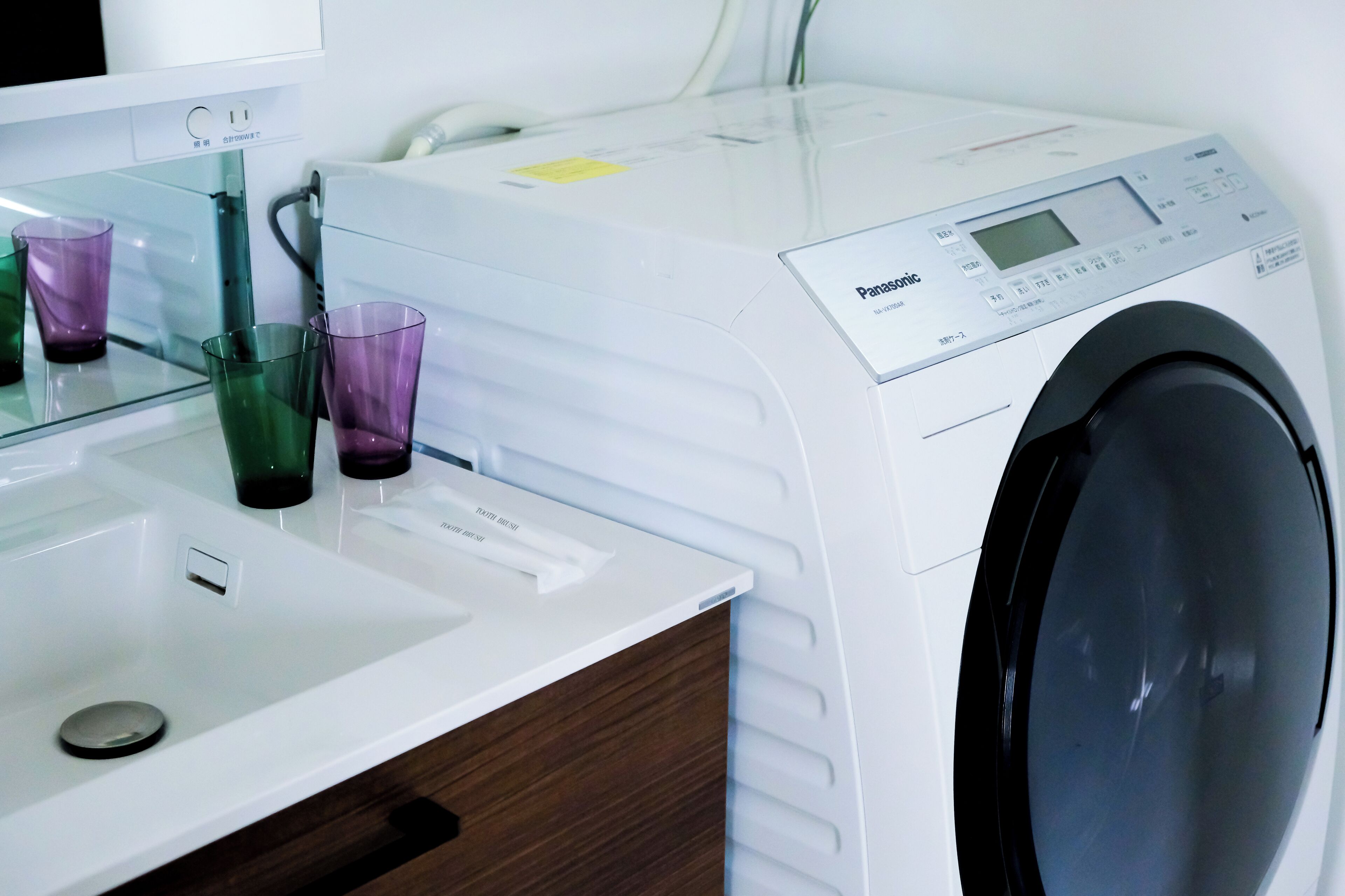 Ein moderner Waschraum mit einer weißen Waschmaschine, einem Waschbecken und zwei Glasbehältern.