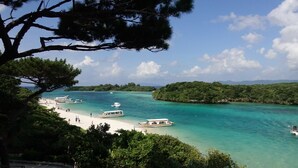 Zona costera con barcos amarrados cerca de una playa arenosa, rodeada de exuberante vegetación y aguas turquesas cristalinas.