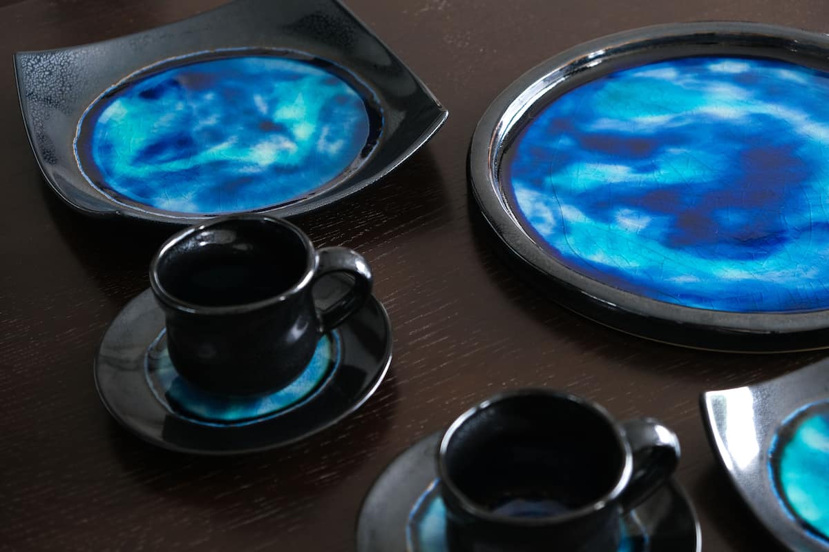 Un tavolo con un centrotavola in vetro blu, due tazze nere e un piattino.