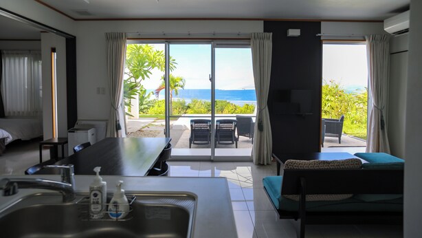 Habitación de hotel con zona de comedor, sofá y vista al océano.