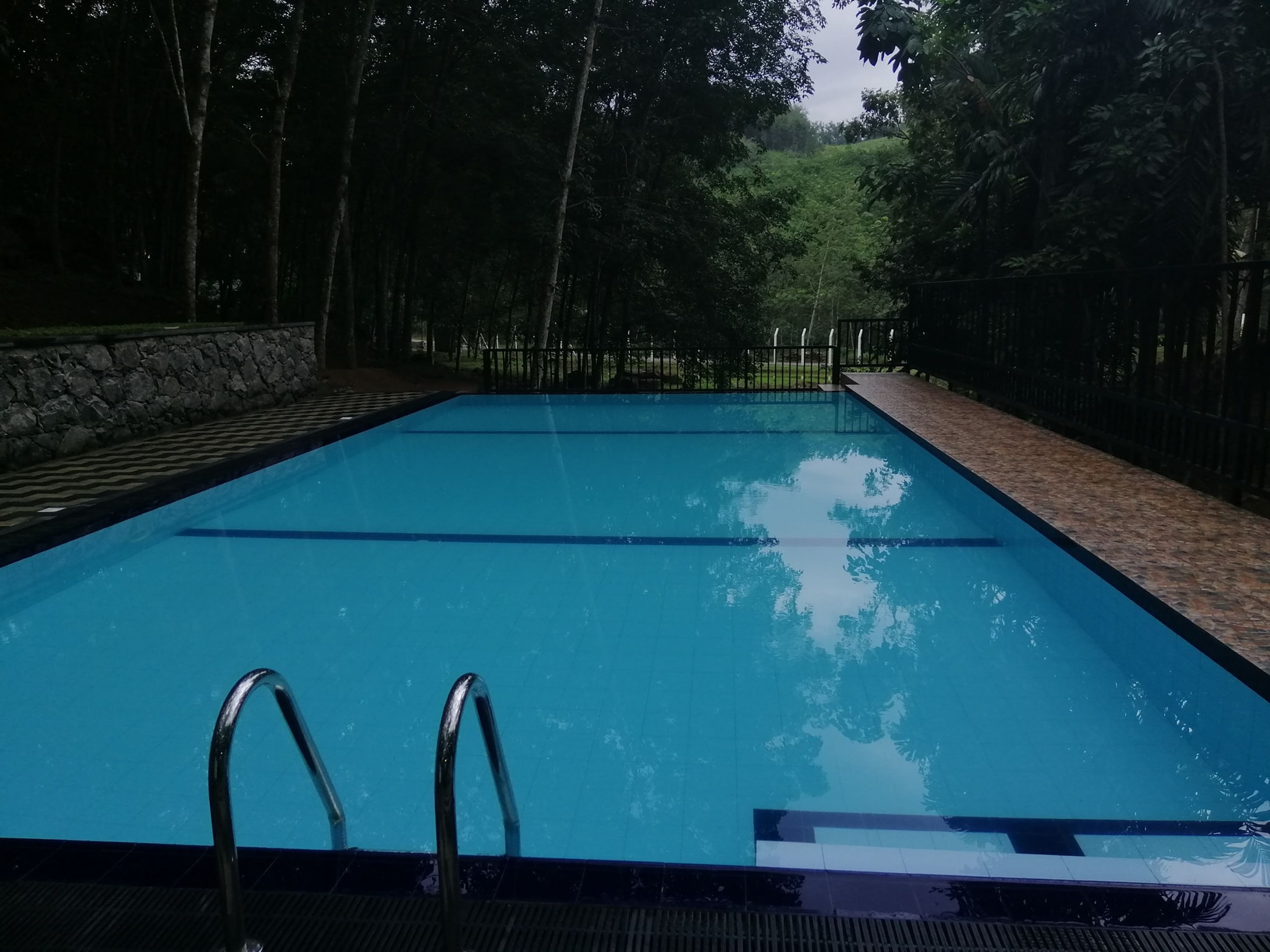 Une piscine rectangulaire à l’eau d’un bleu limpide, entourée d’un mur de pierre et de rampes métalliques.