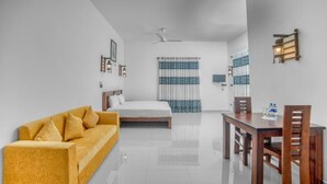 A modern hotel room with a bed, a sofa, a dining table with chairs, and a ceiling fan. - Seethawaka Royal Resort (Hanwella)