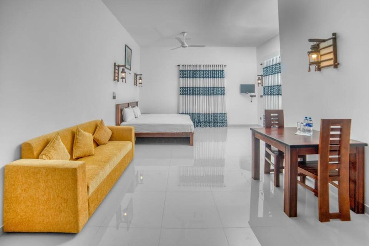 A modern hotel room with a bed, a sofa, a dining table with chairs, and a ceiling fan.