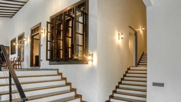A staircase with wooden steps and a marble floor, leading to a landing with a door and a wall-mounted light fixture. - Seethawaka Royal Resort (Hanwella)