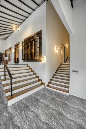 A staircase with wooden steps and a marble floor, leading to a landing with a door and a wall-mounted light fixture. - Seethawaka Royal Resort (Hanwella)