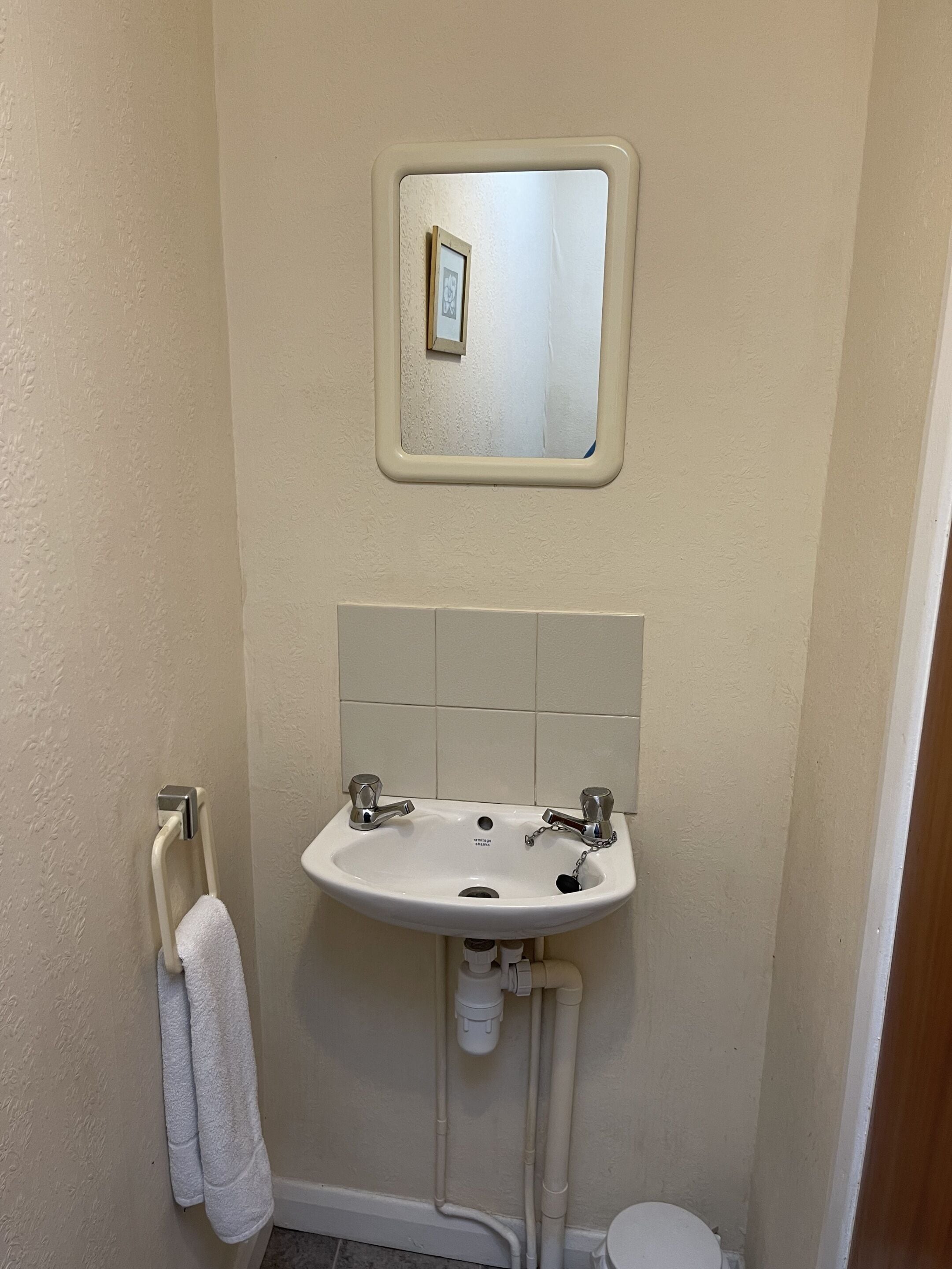 Une salle de bain avec un lavabo blanc, un miroir au-dessus et un porte-serviettes sur lequel est accrochée une serviette.